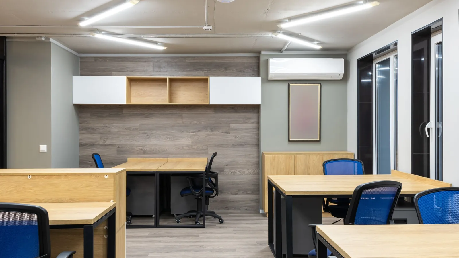 Open space de escritório vazio, com secretárias em ilha e uma unidade de ar condicionado na parede