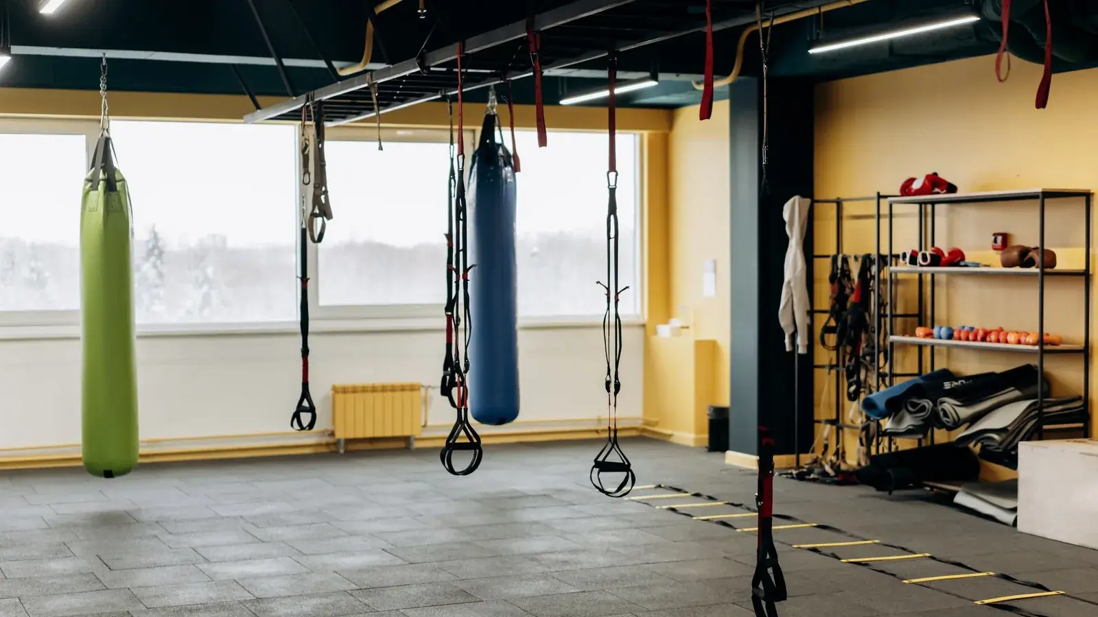Sala de treino de ginásio vazia, com sacos de boxe suspensos e a estrutura do teto à vista