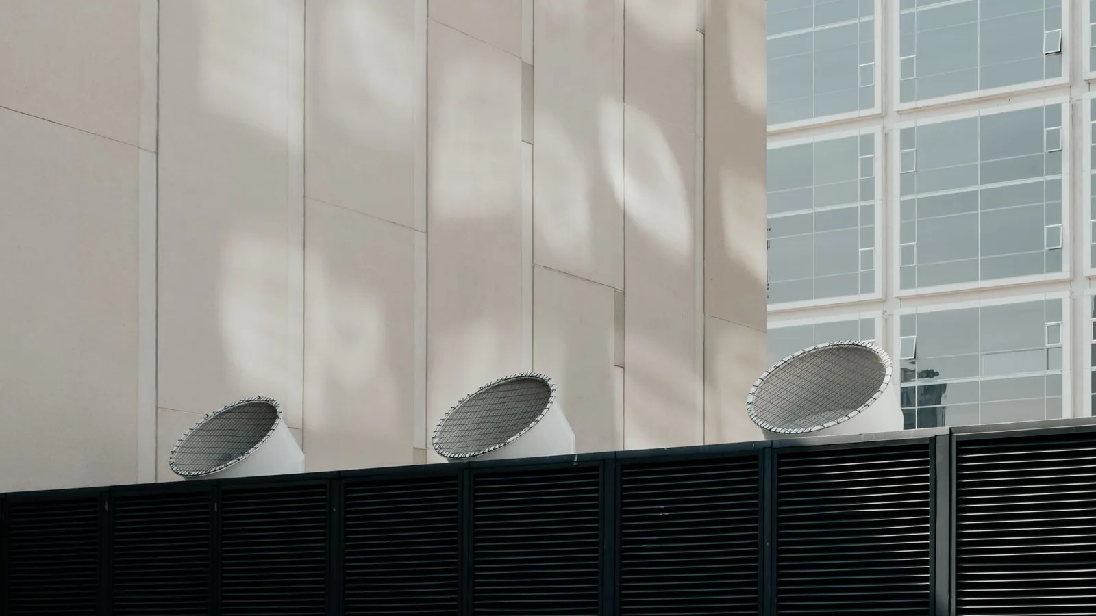 Bocas de exaustão de ar alinhadas sobre grelhas de ventilação na fachada de um edifício comercial