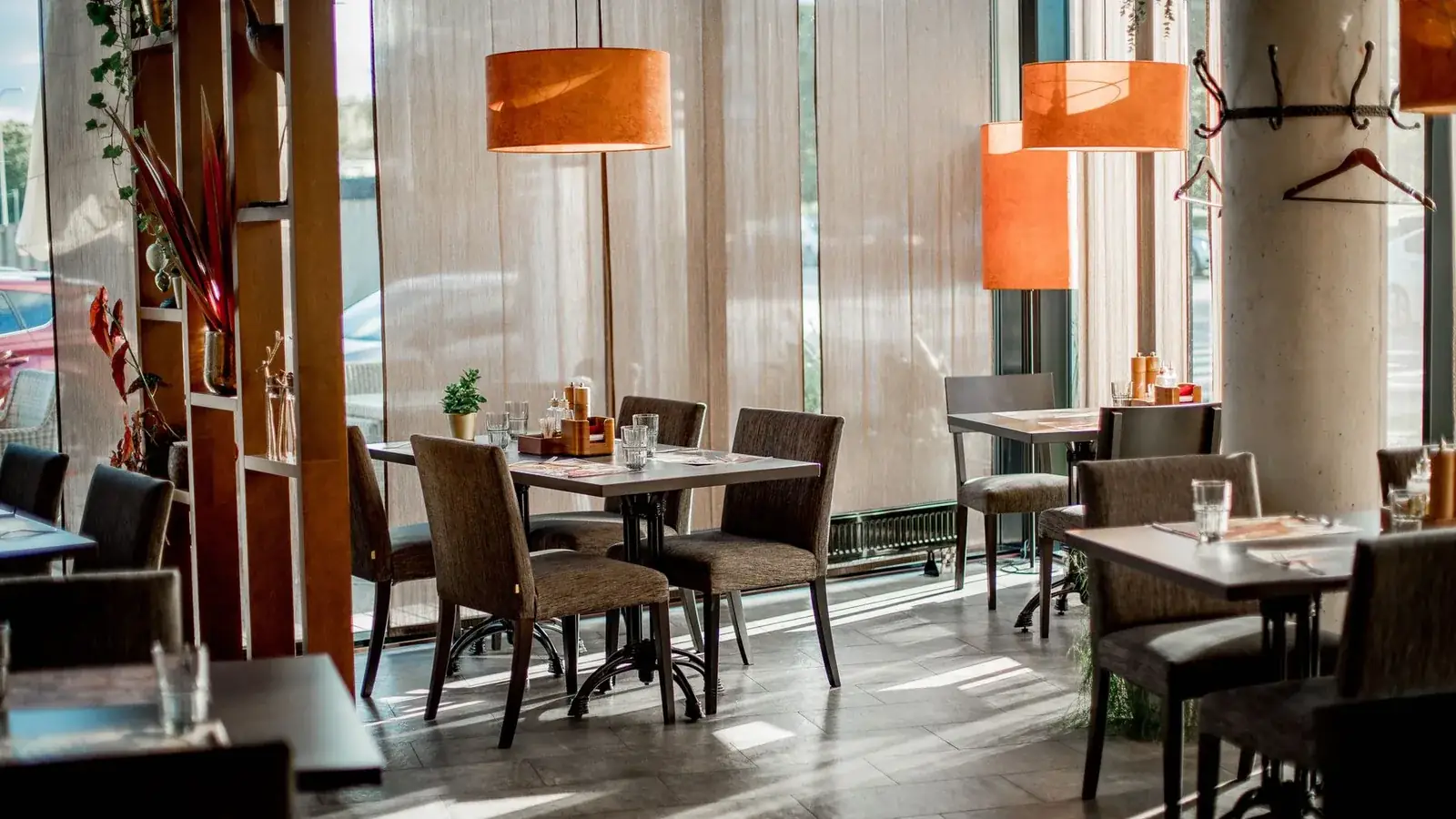 Sala de restaurante vazia com mesas postas junto a uma parede de vidro ao sol